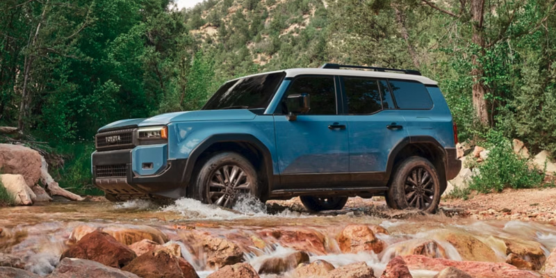 Blue Toyota Land Cruiser driving through a rocky stream.