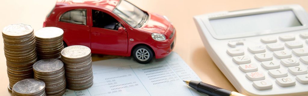 A toy red car next to stacks of coins and a calculator on a financial document.