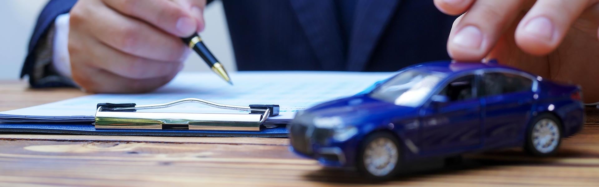 Person signing paperwork next to a blue toy car model